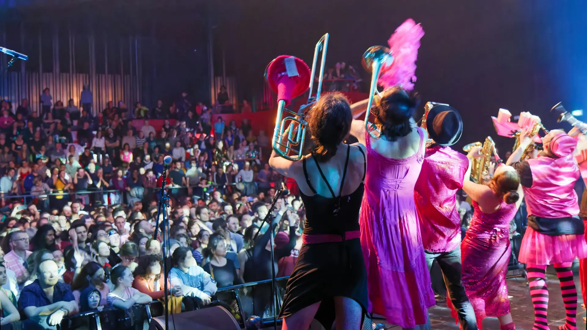 Performers in pink costumes on stage with audience